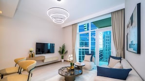 A modern living room with a sofa, chairs, a coffee table, a TV, and a large window with curtains. - Luxury 1BR in Business Bay (Dubai)