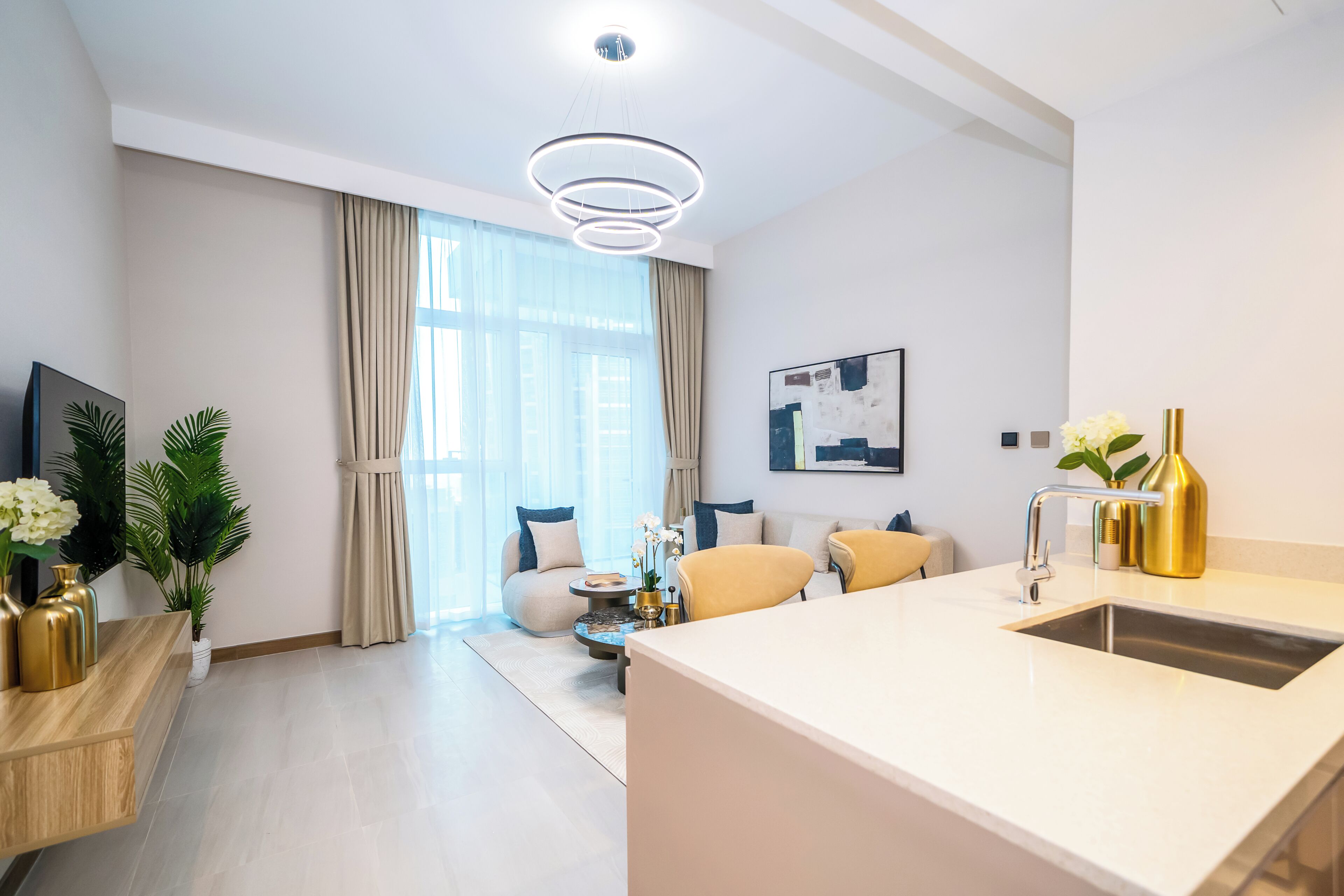 A modern living room with a sofa, a coffee table, and a kitchen area with a sink and a pendant light.