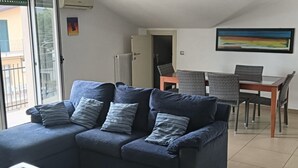 Un salon avec un canapé bleu, une table basse en verre, une table à manger avec des chaises et un tableau accroché au mur.