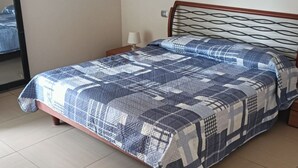 Un lit avec une couvre-lit à motifs géométriques, une table de chevet avec une lampe et un miroir au mur.