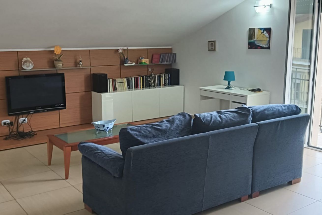 A living room with a sofa, a coffee table, a TV, a bookshelf, and a desk with a lamp.