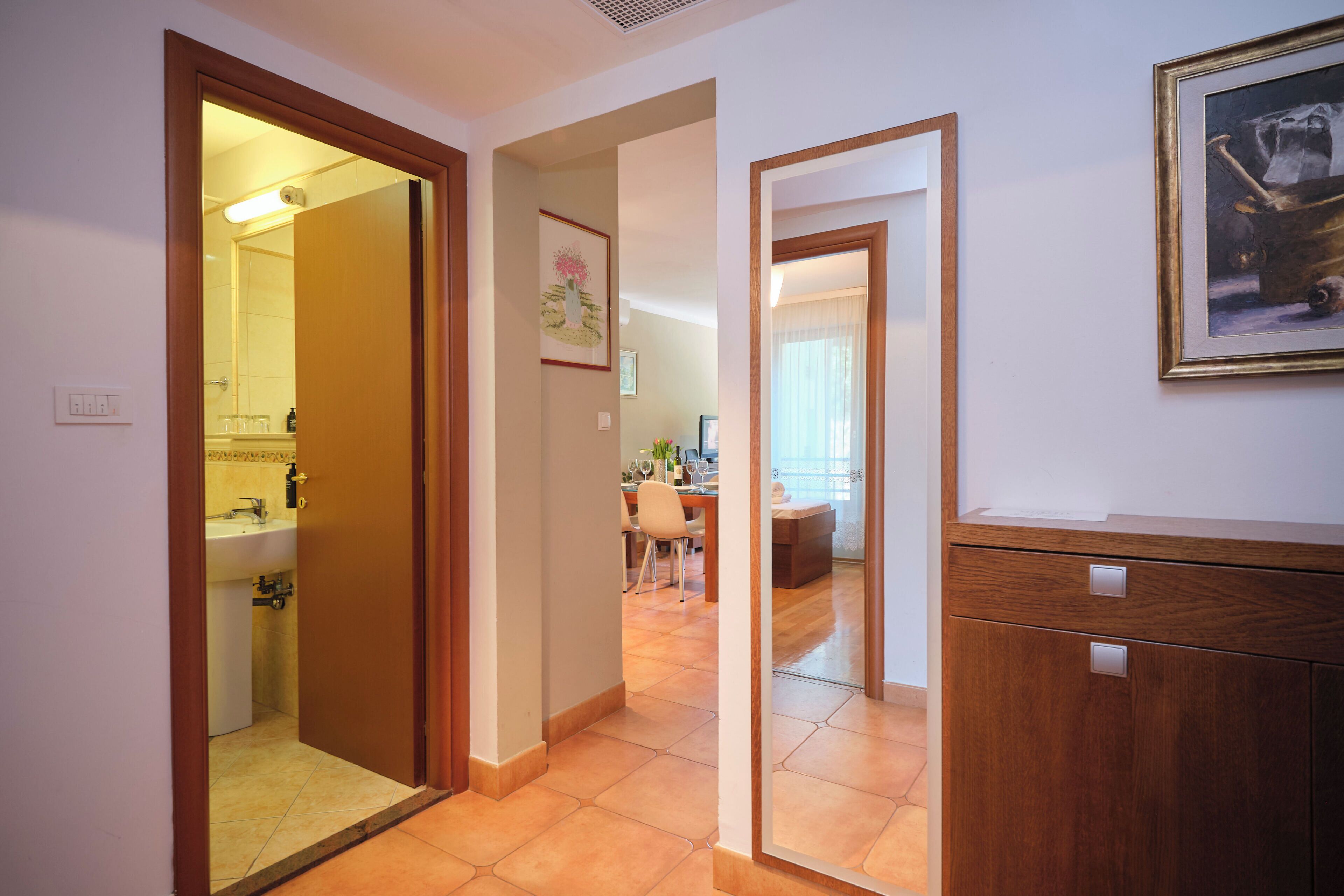 Un couloir avec une porte en bois donnant sur une salle de bain, un coin repas avec une table et des chaises, et un meuble en bois avec des tiroirs.