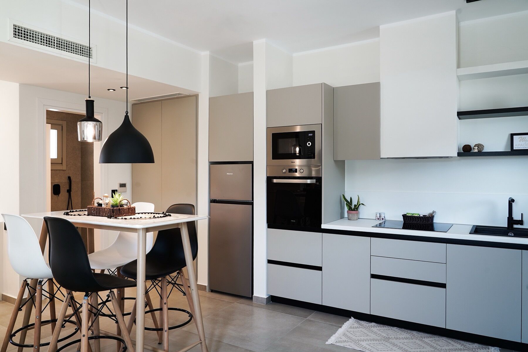 A modern kitchen with a dining area, featuring a black pendant light, a stainless steel oven, and a built-in microwave.