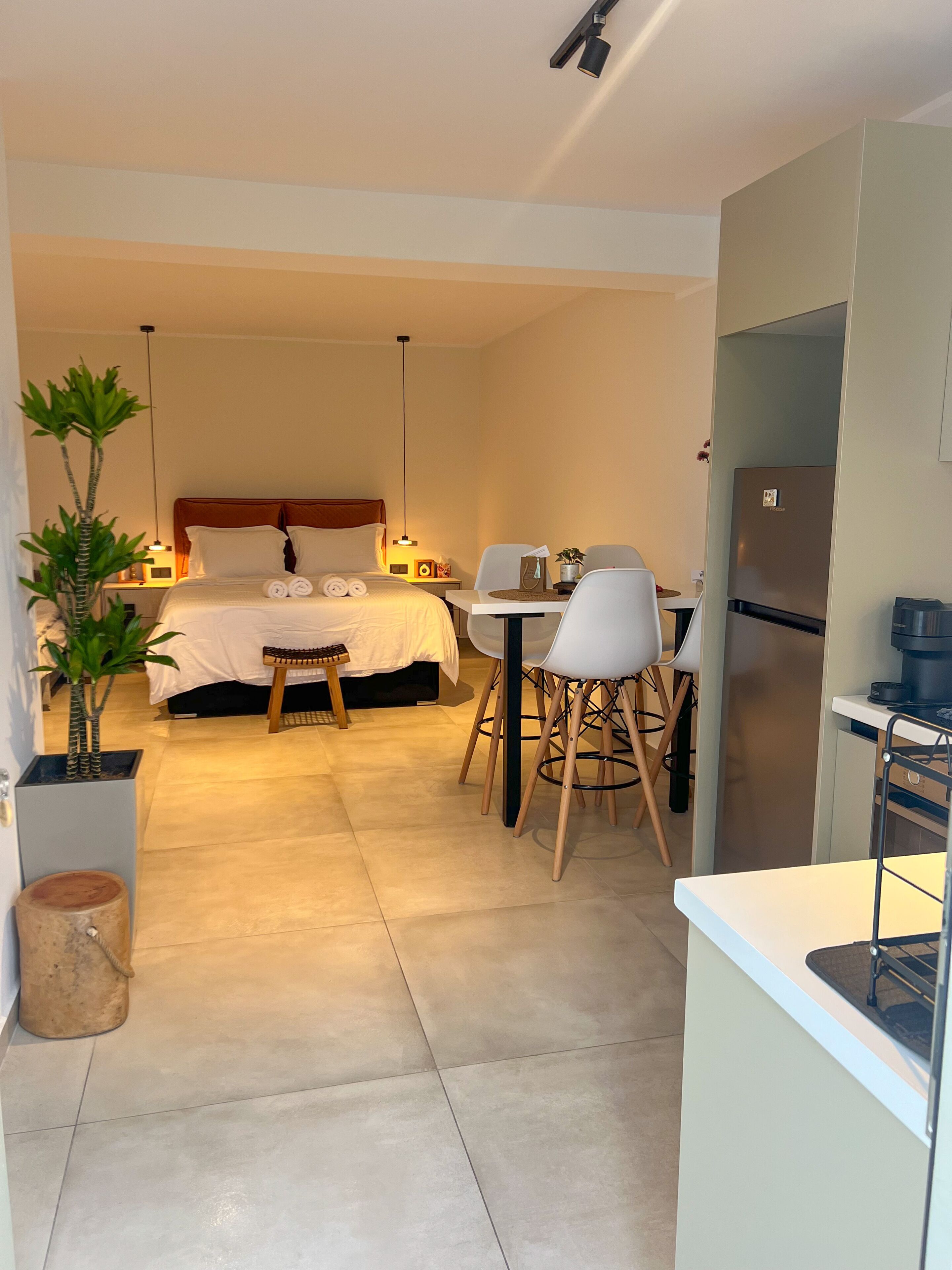 A modern hotel room with a bed, bedside table, lamp, and a dining area with chairs and a table.