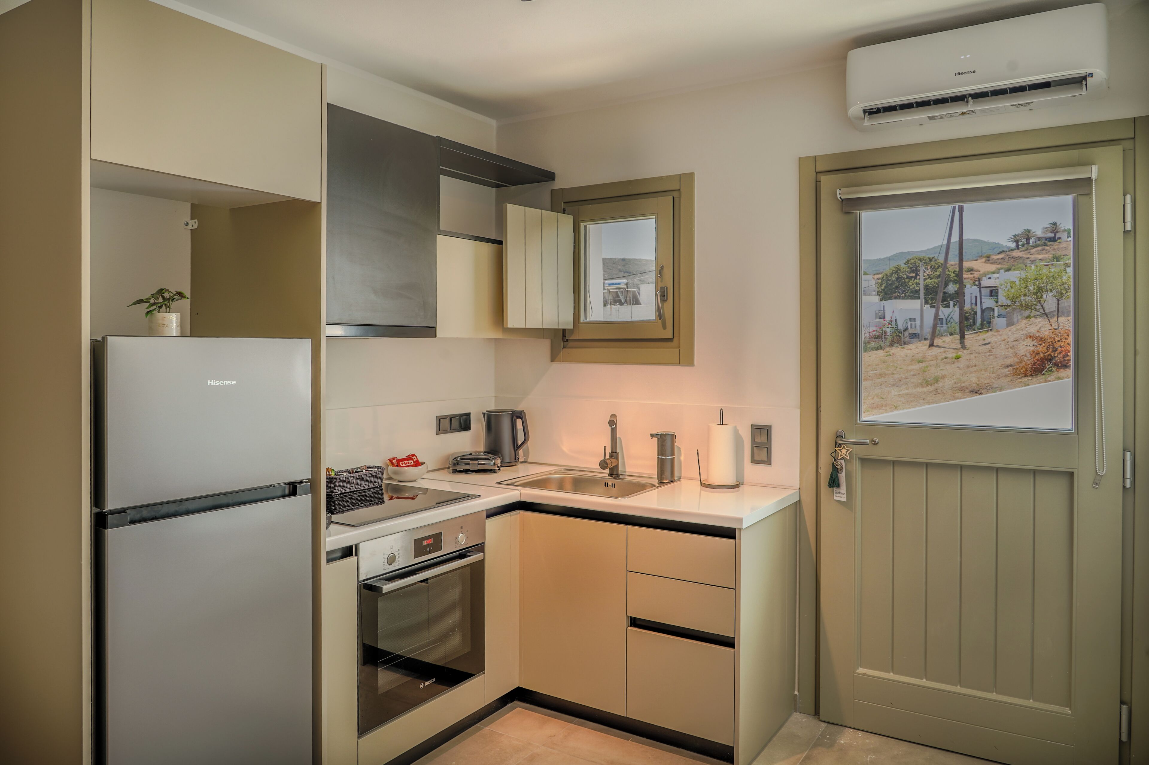 A compact kitchen with a refrigerator, oven, sink, and a window with a view of a hillside.