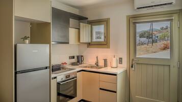 A compact kitchen with a refrigerator, oven, sink, and a window with a view of a hillside.