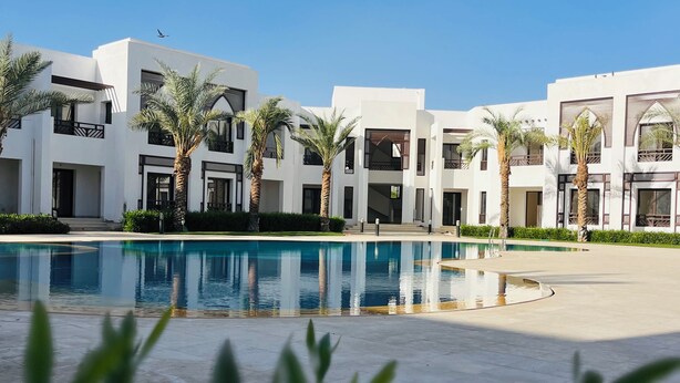 Ein modernes Hotel mit Swimmingpool, Palmen und blauem Himmel.