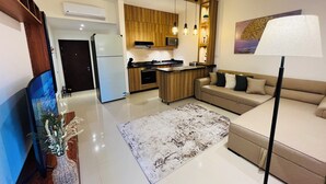 Ein modernes Wohnzimmer mit Sofa, Couchtisch, Fernseher und Küchenzeile mit Holzschränken sowie einem Deckenventilator.
