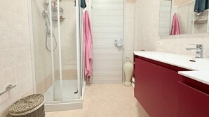 Un baño con ducha, lavamanos, espejo y toallero.