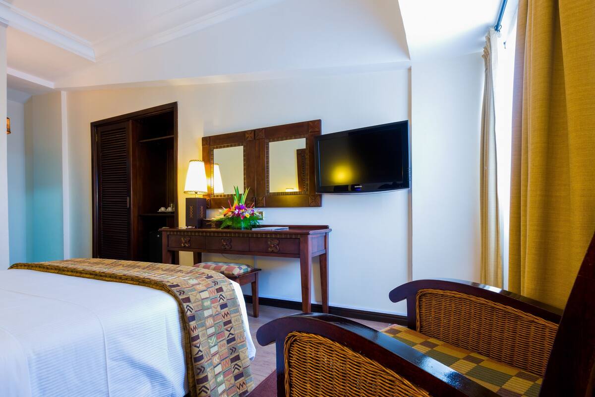 A hotel room with two beds, a desk with a lamp and flowers, a television, and a chair.