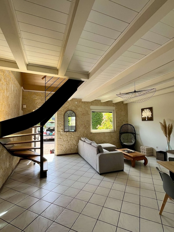 A spacious living area with a staircase, a sofa, a wooden coffee table, and a window with a view of greenery.