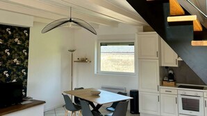 A modern kitchen with white cabinets, a dining area with a wooden table and chairs, and a staircase with black railings and wooden steps.