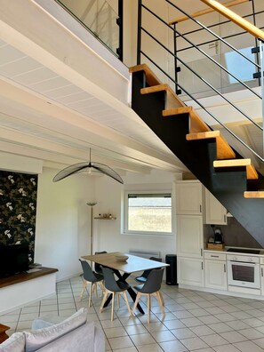 A modern kitchen with white cabinets, a dining area with a wooden table and chairs, and a staircase with black railings and wooden steps.
