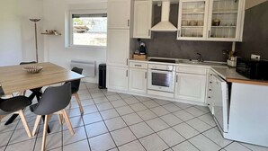 A compact kitchen with white cabinets, a dining table with chairs, a window, and a radiator.