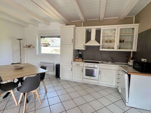 Una cocina compacta con armarios blancos, una mesa de comedor con sillas, un ventanal y un radiador.