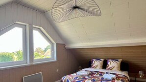 A bedroom with a large window, a bed with a colorful bedspread, a unique ceiling light, and a wooden headboard.