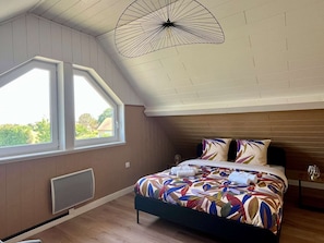 A bedroom with a large window, a bed with a colorful bedspread, a unique ceiling light, and a wooden headboard.
