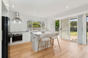 A modern kitchen with a central island, bar stools, and a sliding glass door leading to a garden. - Paw-fect Family Retreat: 4BR Home in Connolly (Connolly)