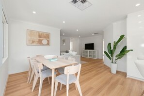 A modern living room with a dining area, a flat-screen TV, and a potted plant. - Paw-fect Family Retreat: 4BR Home in Connolly (Connolly)