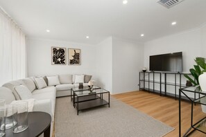 A modern living room with a sofa, coffee table, TV, and artwork on the wall. - Paw-fect Family Retreat: 4BR Home in Connolly (Connolly)