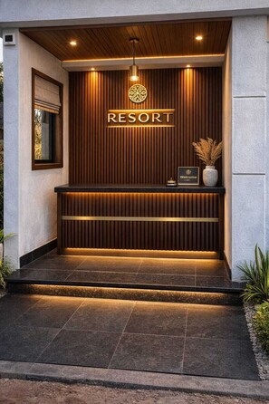 A reception desk with a wooden panel backdrop, a 'RESORT' sign, a welcome sign, and a potted plant. - Zista Inn (Shrivardhan)