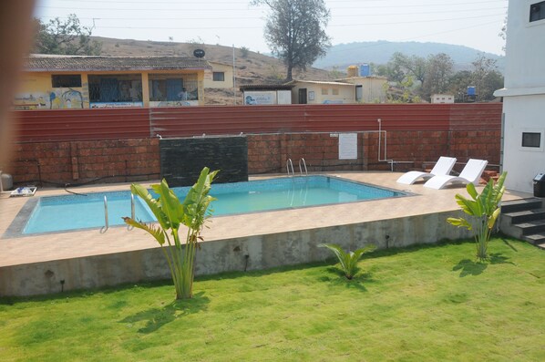 A rectangular swimming pool with a brick wall and a grassy area with lounge chairs. - Zista Inn (Shrivardhan)