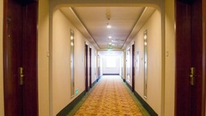 Un pasillo de hotel con piso alfombrado, puertas de madera y pared de color claro.