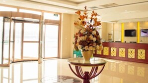 Un vestíbulo de hotel con una recepción, una lámpara de araña grande y una mesa de vidrio con un jarrón decorativo.