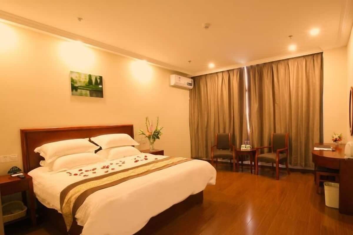 Quarto de hotel com cama, escrivaninha, cadeira e janela com cortinas.