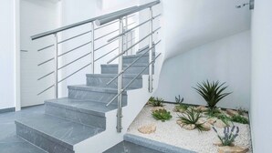 Una escala moderna amb baranes metàl·liques i graons de marbre, que condueix a un espai de descans amb una petita zona verda.