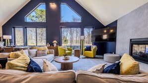 Un salon spacieux avec un haut plafond, de grandes fenêtres, un téléviseur à écran plat et une cheminée.