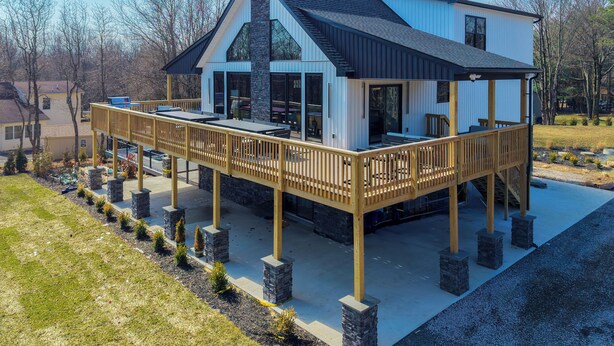 Une maison moderne dotée d’une grande terrasse, de piliers en pierre et d’une cheminée en pierre.