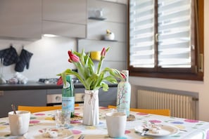 A dining table with a floral tablecloth, a vase with red tulips, and bottles of water and tea. - 'Kikosa House' Apartment with Private Terrace, Wi-Fi and Air Conditioning (Castelnuovo del Garda)