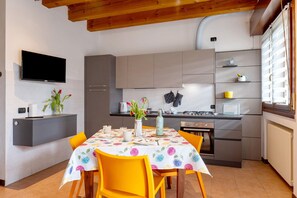 Una cucina moderna con mobili grigi, una TV a schermo piatto e un'area pranzo con tavolo imbandito per due persone.