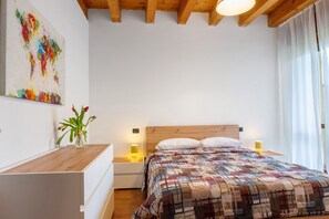 Una camera da letto con una testiera in legno, una coperta a motivi, lampade sui comodini, un tavolino notte, un vaso con fiori e un quadro appeso al muro.