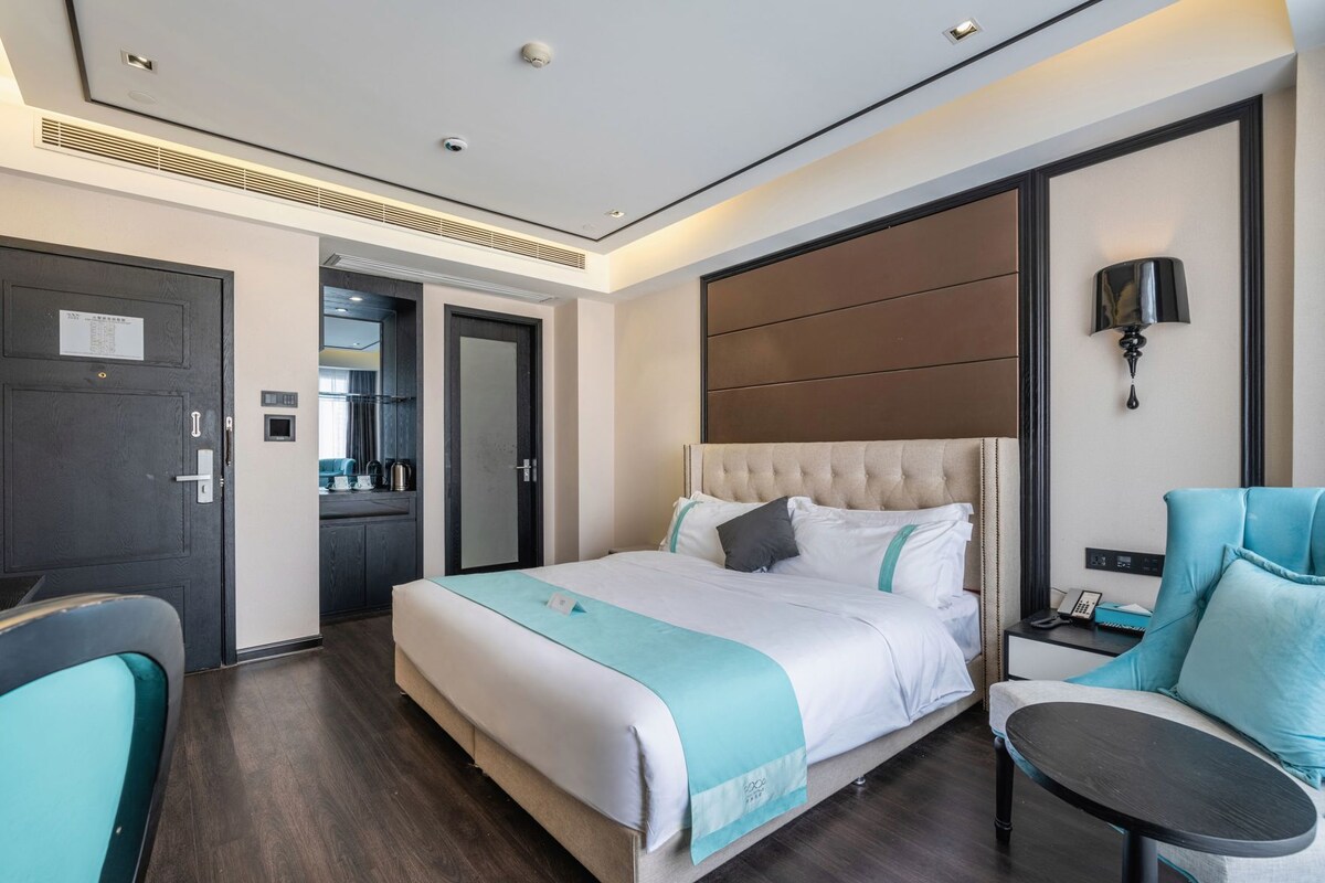 A modern hotel room with a large bed, a desk, a chair, and a small table.