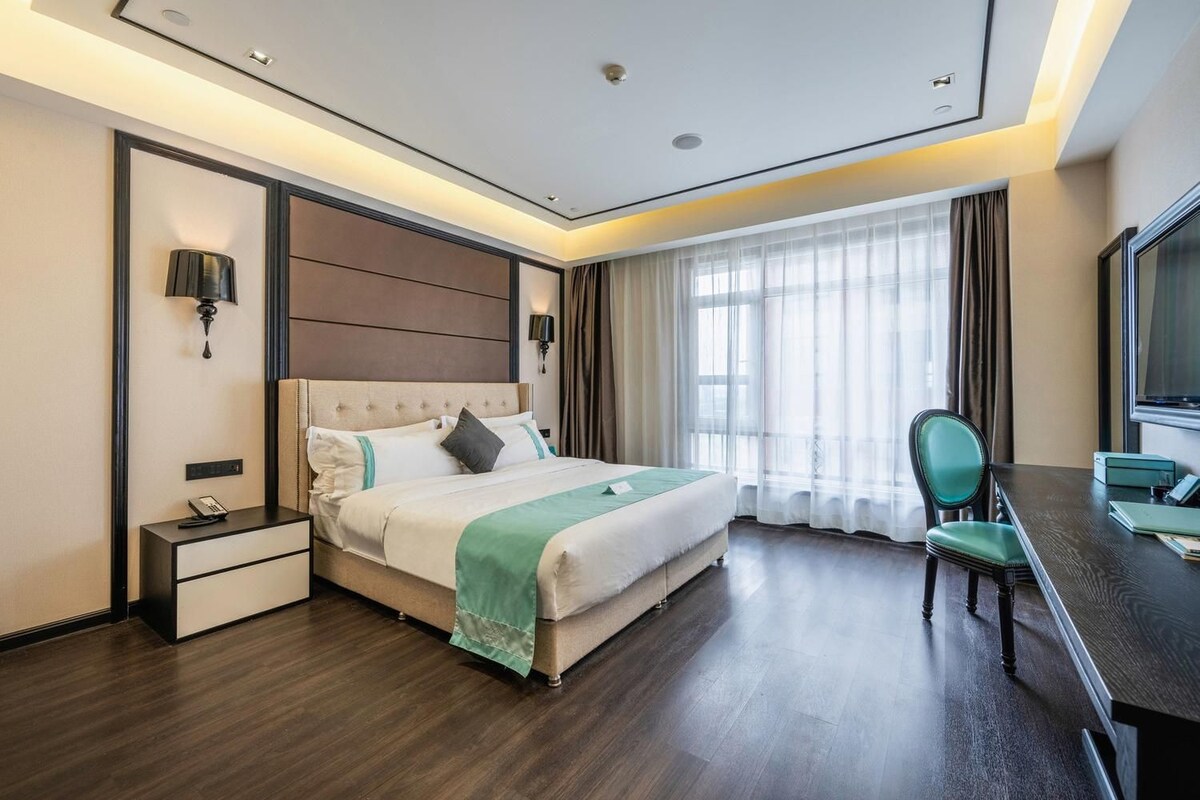 A hotel room with a bed, bedside table, desk, chair, and a TV.