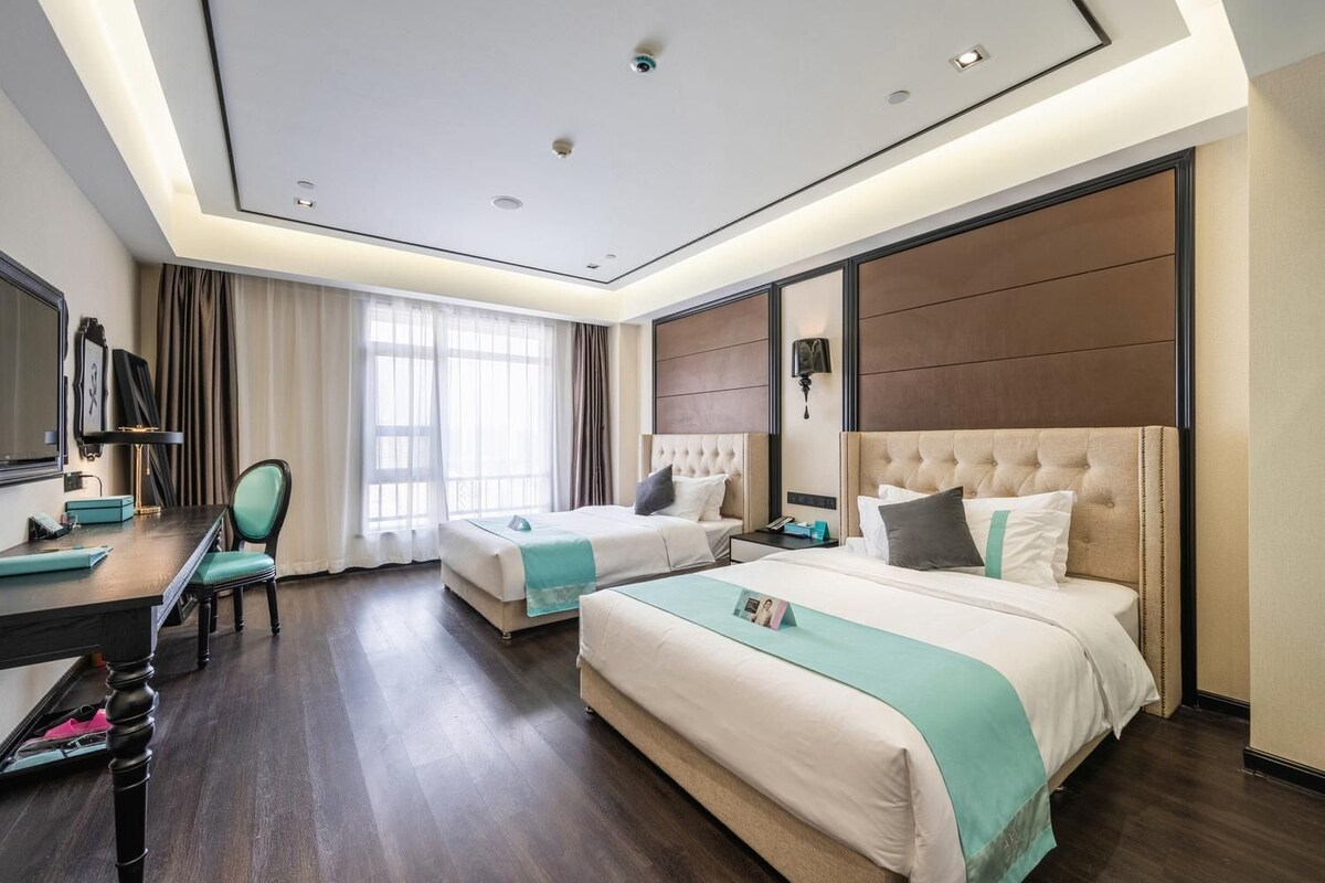 A hotel room with two beds, a desk, a chair, and a television.