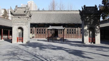 A traditional building with a tiled roof and wooden doors, a stone bench in the center, and a clear sky.