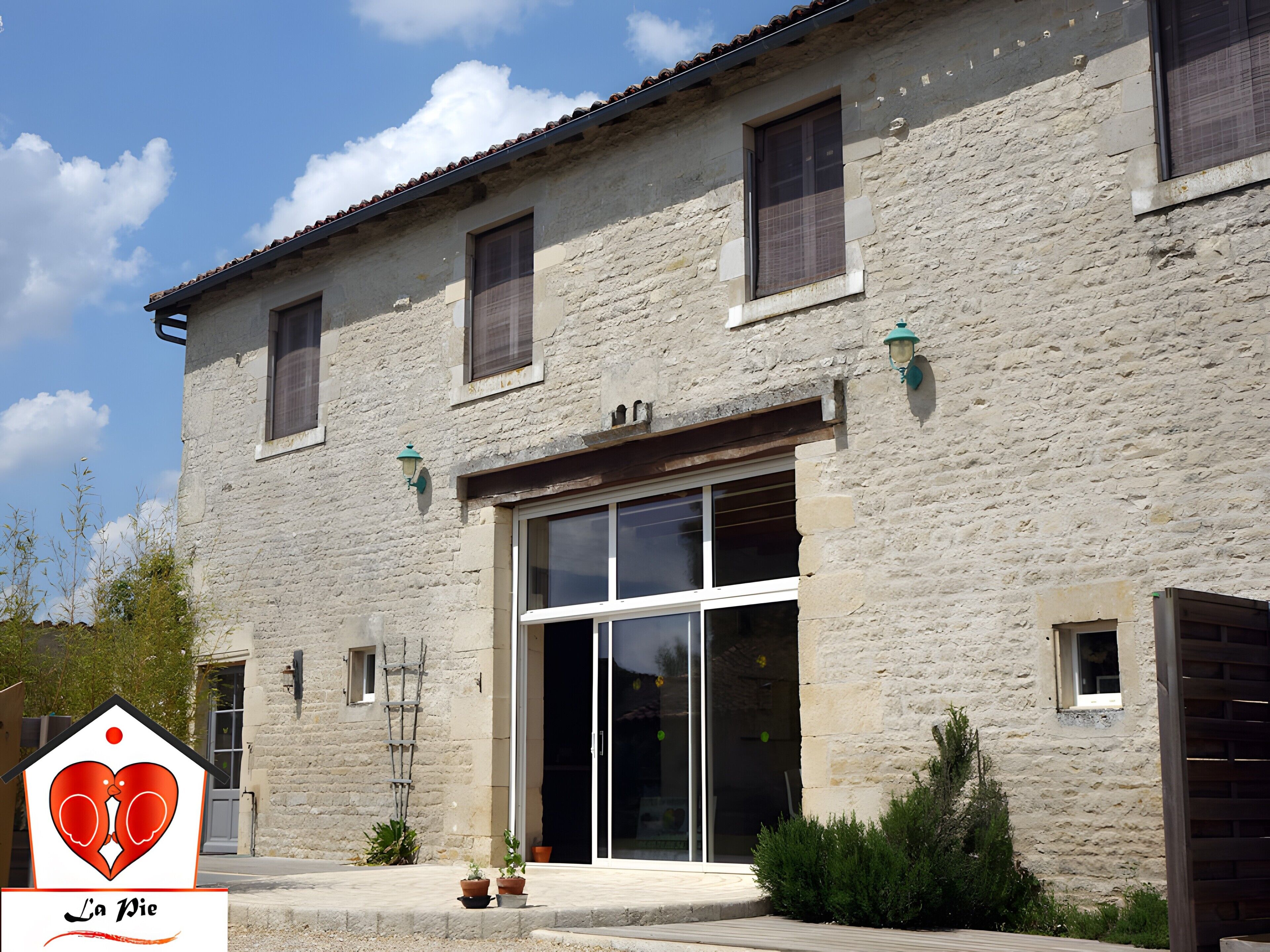 Un edificio in pietra con un'ampia porta in vetro, piccole finestre e un tetto in tegole.
