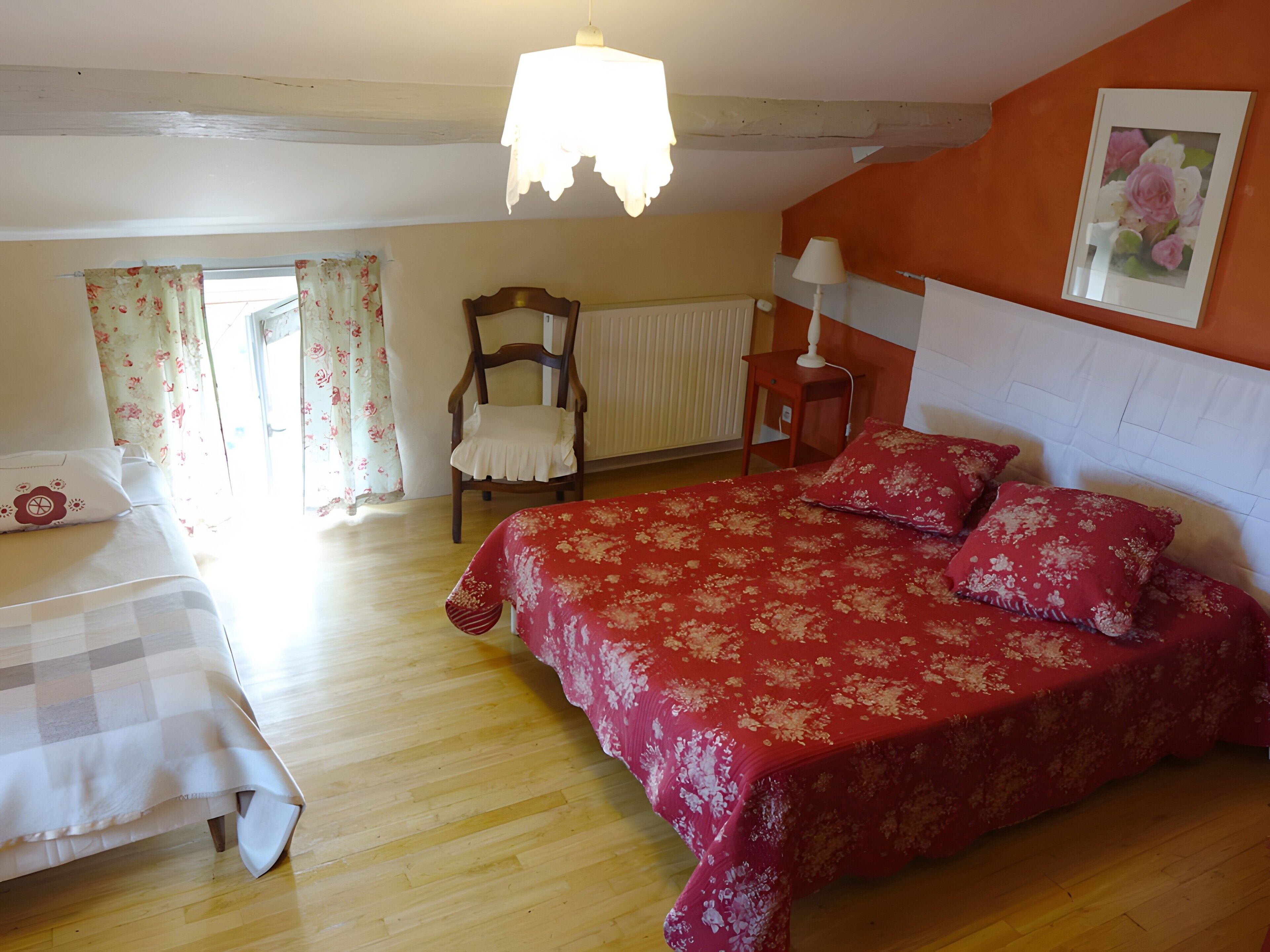 A bedroom with a bed, a chair, a table, a lamp, and a window with curtains.