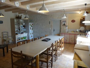 Una cuina àmplia amb un gran taula de dinar, cadires de fusta, il·luminació penjant i una paret de pedra.