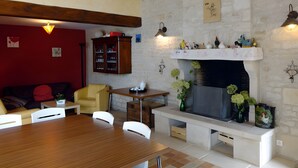 Ein gemütliches Wohnzimmer mit Kamin, Holzbalken, einer roten Wand, einem Esstisch und einem Bücherregal.