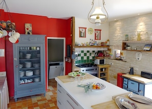 Une cuisine avec un mur rouge, un meuble bleu, un plan de travail blanc et un luminaire suspendu.