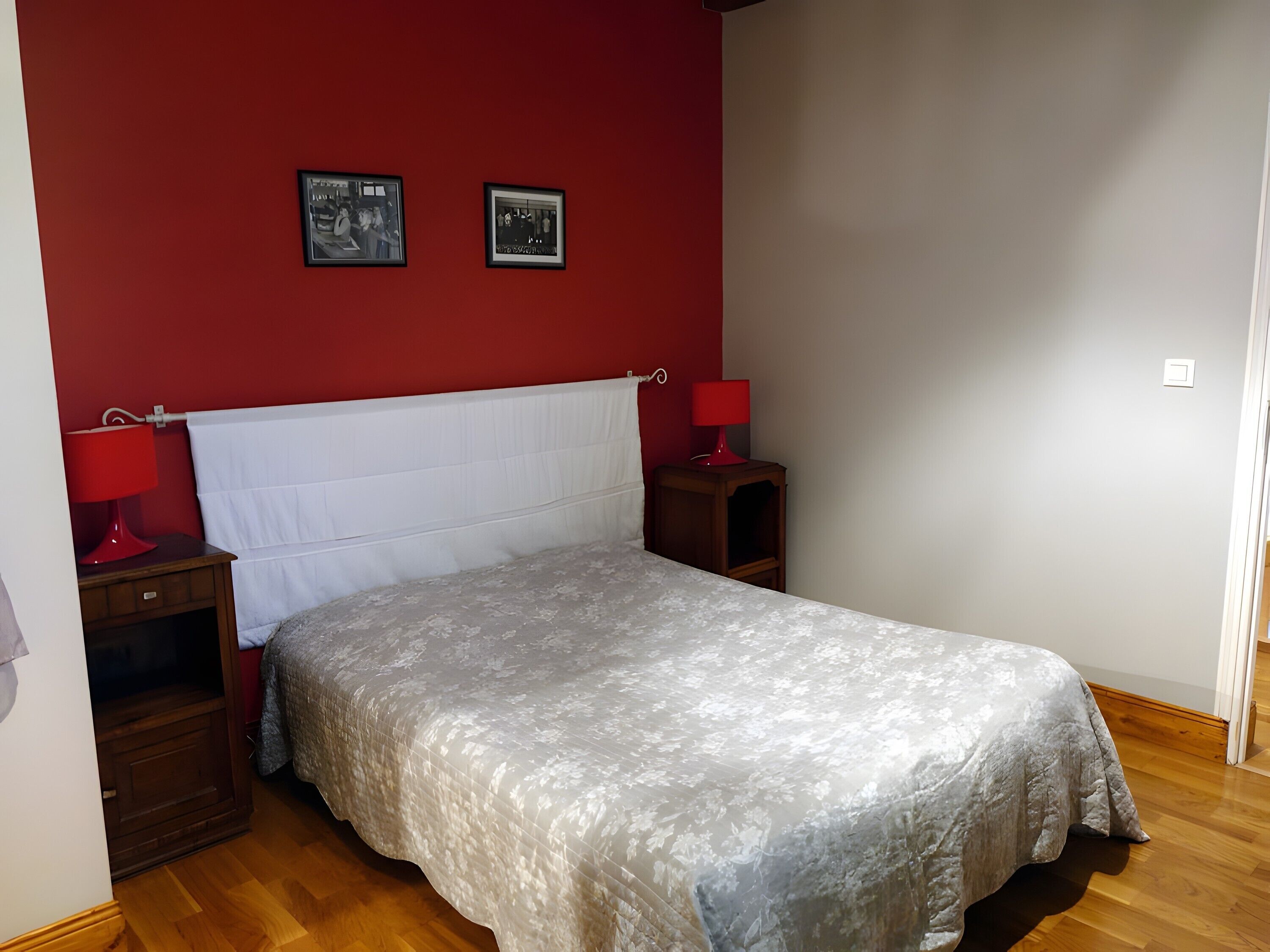 Una camera da letto con un letto, due comodini, un muro rosso e due quadri incorniciati.