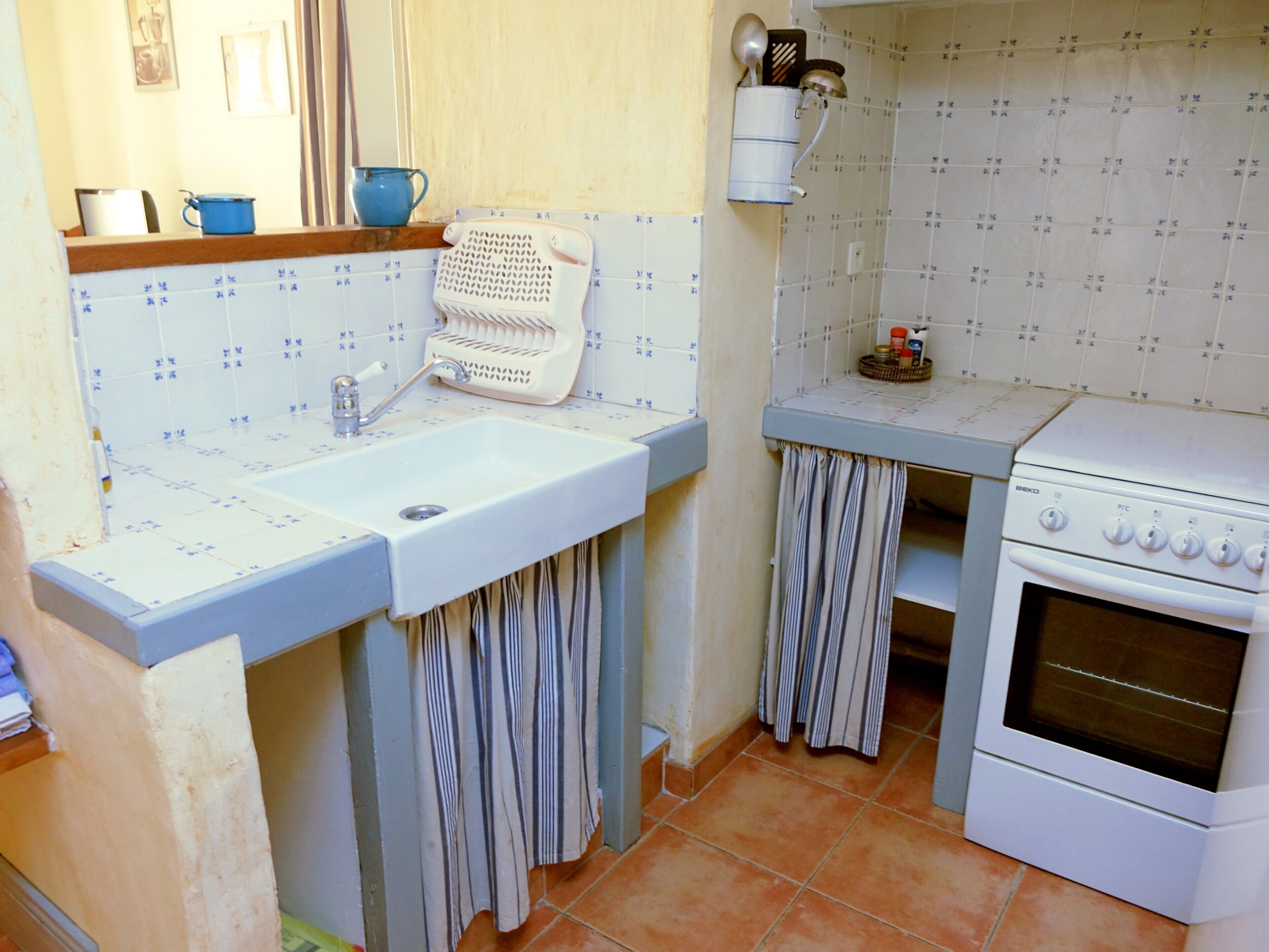 Een keuken met een spoelbak, fornuis en betegelde spatwand.