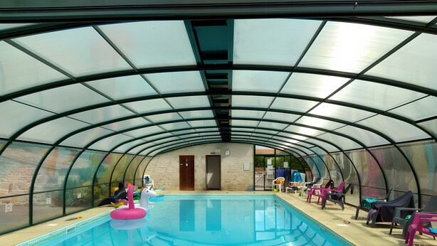 Una piscina interior con techo de vidrio, zona de deck de madera y puerta que da a una habitación contigua.