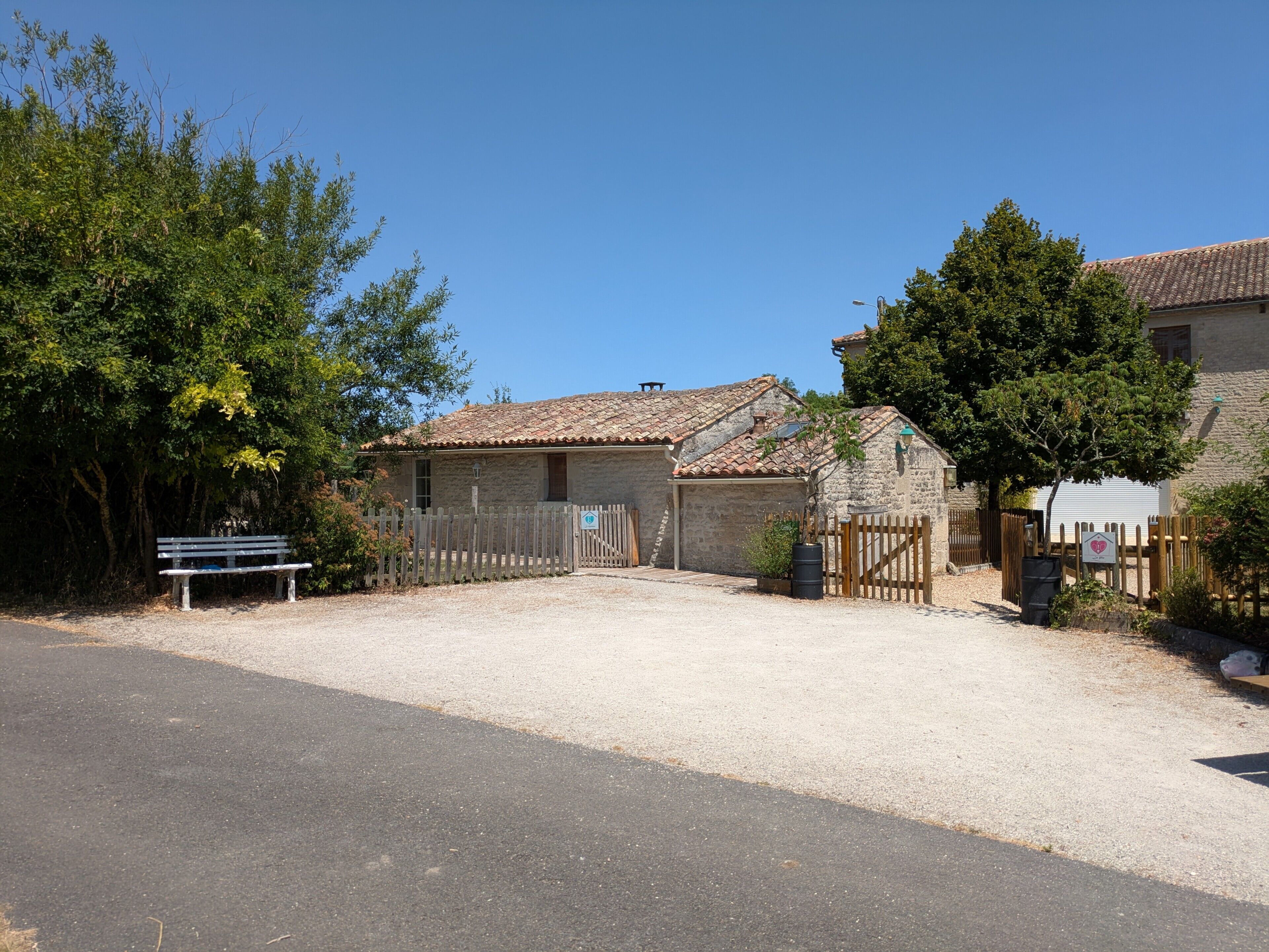 Un bâtiment en pierre avec un toit en tuiles, une allée en gravier et une clôture en bois.