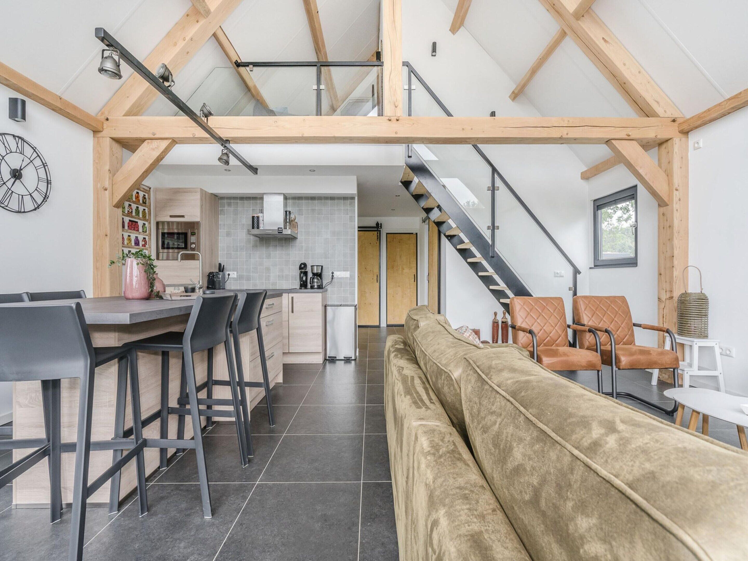A modern interior with a kitchen, dining area, and living space, featuring a high ceiling and exposed beams.