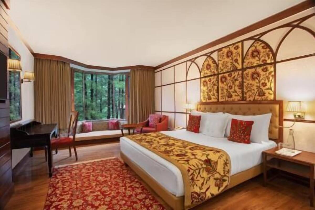 A hotel room with a large bed, a desk, a chair, and a view of the forest.